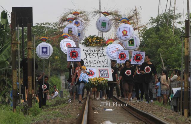Warga membawa spanduk bergambar partai politik peserta pemilu 2014 di rel kereta api daerah Nusukan Solo, Selasa (25/3). Aksi tersebut mengajak warga di pinggiran rel kereta api untuk datang ke TPS pada 9 April 2014 mendatang.