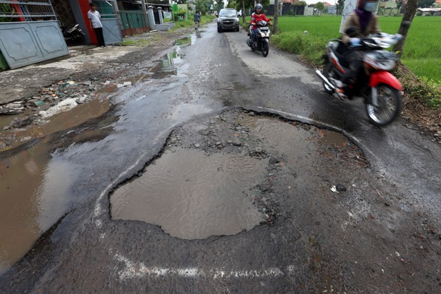 Warga melintasi jalan berlubang yang tergenang air hujan di Jl. Pakel Banyuanyar, Banjarsari, Solo, Rabu (6/4/2016). Coretan cat semprot pada tepi jalan berlubang tersebut menjadi tanda dan peringatan bagi pengendara agar tidak nekat melintasi karena rawan mengakibatkan kecelakaan. (Ivanovich Aldino/JIBI/Solopos)