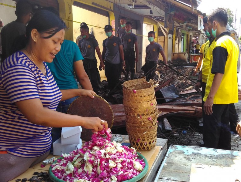 Seorang pedagang Pasar Bendungan kembali berjualan di depan kiosnya yang terbakar pada Selasa (19/4) kemarin. Sejumlah anggota kepolisian tampak sedang membersihkan puing-puing bangunan pasar sejak Rabu (20/4/2016) pagi. (Rima Sekarani I.N./JIBI/Harian Jogja)