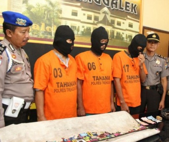 Aparat Polres Trenggalek menunjukkan tiga nelayan (memakai penutup muka) yang digerebek saat berjudi di tempat parkir wisata Pantai Prigi. (tribatanewsjatim.com)