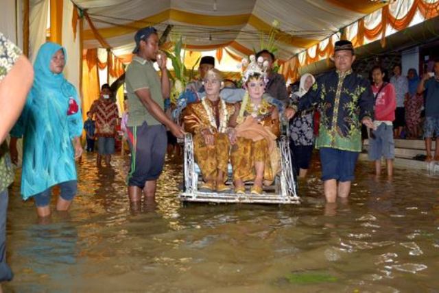 Sepasang mempelai di Desa Karangan, Kecamatan Balong, Ponorogo, Anggi Vicky Angelina dan Indra Kiki Harianto, naik becak saat resepsi pernikahan mereka dalam kondisi banjir, Selasa (12/4/2016). (Facebook-Melaz Pol)