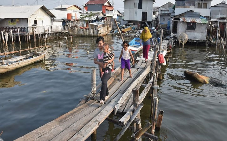 Warga berjalan di atas jembatan kayu di perkampungan nelayan Muara Angke, Jakarta Utara, Sabtu (31/7/2021). (ANTARA FOTO/Indrianto Eko Suwarso)