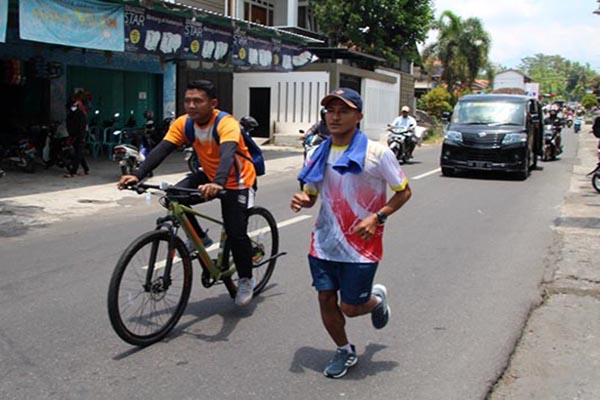Mustakim dikawal rekannya berlari untuk melaksanakan nazarnya melintas di Krajan, Jatinom, Klaten, Senin (18/10/2021). (Solopos/Taufiq Sidik Prakoso)